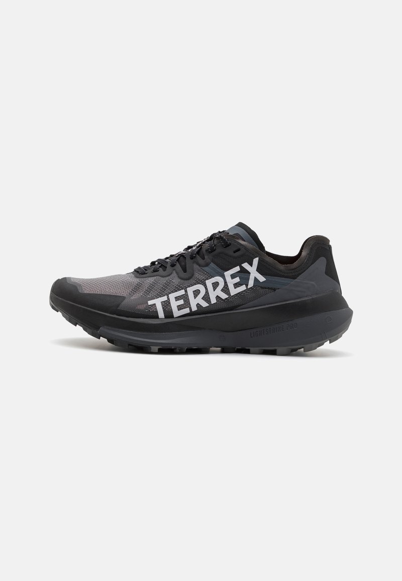 Black athletic shoe with gray mesh fabric and bold white "TERREX" branding. Features a textured sole for traction and a streamlined design.