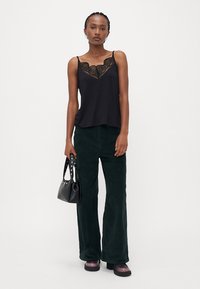 Zwarte cami met kantafwerking, gecombineerd met groene fluwelen uitlopende broeken. Gecombineerd met een kleine zwarte tas en plateau schoenen.