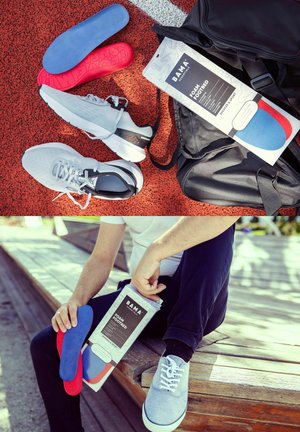 Grå sportssko, røde og blå skumindlægssåler, sort rygsæk og person, der holder emballage til indlægssåler udendørs på rød løbebane og træbænk.