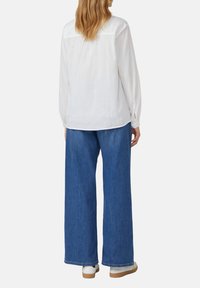 Weißes Langarmhemd mit Rückenschulterdetail, kombiniert mit weit geschnittenen blauen Jeans und weißen Sneakers mit beiger Sohle.