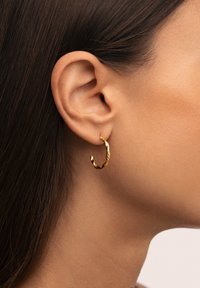 Pendiente de aro de oro con un diseño texturizado. Forma circular, tamaño mediano, con un sutil acabado martillado. Lleva en el lóbulo de la oreja.