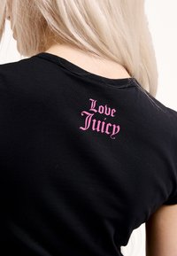 Fekete rövid ujjú póló, amelynek hátulján rózsaszín "Love Juicy" felirat található. Az anyag puhanak és testhez simulónak tűnik.