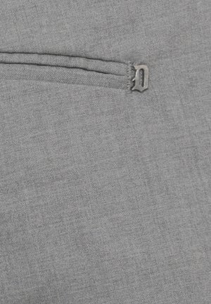 Tessuto grigio con una piccola lettera metallica "D" attaccata vicino a una tasca o cucitura orizzontale cucita.