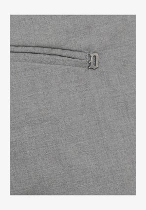 Tessuto grigio con una piccola lettera metallica "D" attaccata vicino a una tasca o cucitura orizzontale cucita.