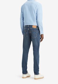 Camisa de manga larga azul claro combinada con jeans de mezclilla azul medio. Los jeans cuentan con un parche de cuero en la parte trasera y un corte recto en las piernas.