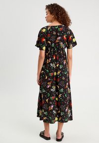 Robe noire à manches courtes avec un motif floral et céleste coloré. Taille élastique, longueur midi et coupe ample. Sandales à glisser noires.