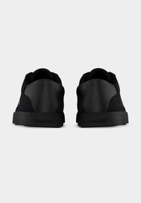 Paire de baskets noires Calvin Klein vues de dos, avec des empiècements en cuir lisse sur le talon et des semelles avec logo, sur fond blanc.