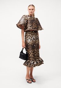 Leopardmønstret to-delt antrekk med metallisk finish. Kort topp med brede ermer, tettsittende skjørt med bølget kant. Svart håndveske.