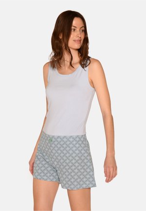 Donna con capelli castani fino alle spalle, che indossa una canotta grigio chiaro e pantaloncini grigi con fantasia, che guarda verso destra.