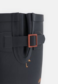 Seau en caoutchouc noir avec une surface texturée, doté d'une boucle carrée marron et de motifs de parapluies orange. Conception robuste avec un bord supérieur pliable.