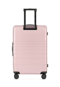 Hartschalenkoffer in zartem Rosa mit vertikalen Rillen, schwarzem Griff und vier Rollen für Mobilität. Verfügt über einen Seitengriff zum Anheben.