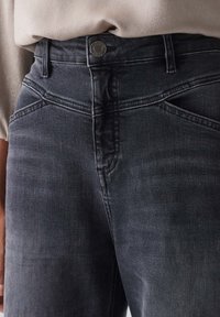 Vaqueros gris de tiro alto con una textura suave, diseño de cinco bolsillos y cierre de botón metálico en la cintura.