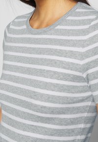 Camiseta a rayas gris y blanca con escote redondo, hecha de tela acanalada. Vista en primer plano que resalta la suave textura y el patrón.