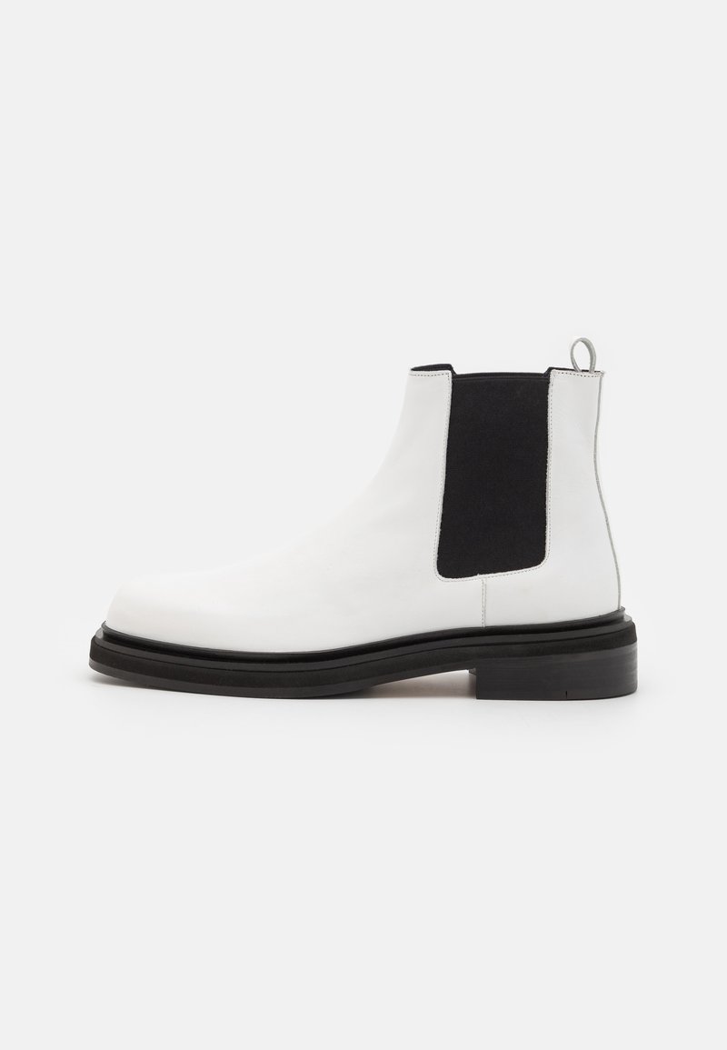 Botte Chelsea en cuir blanc avec panneau élastique noir sur le côté, semelle noire et languette à l'arrière, vue du côté extérieur sur fond blanc.