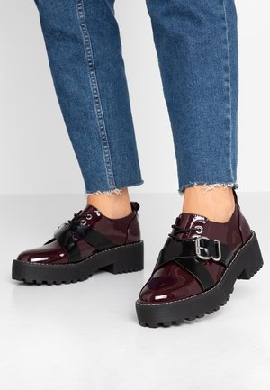 Bordowe lakierowane buty ze skóry z masywną czarną platformą, sznurowane, z ozdobną klamrą z przodu.