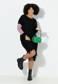 Schwarzes Strickkleid mit Ärmeln im pinken Leopardenmuster, fransigem Saum, kombiniert mit schwarzen Nieten-Stiefeletten und einer grünen, kurzen Handtasche.