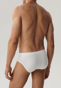Białe bawełniane slipy z miękkim elastycznym pasem, dopasowany krój i gładka tekstura, ukazujące plecy modela męskiego.