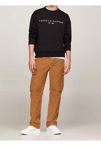 Czarna bluza z logo "TOMMY HILFIGER", zestawiona z beżowymi spodniami typu cargo z bocznymi kieszeniami oraz białymi butami sportowymi. Prosty i casualowy styl.