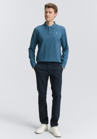 Langærmet blå polo med krave, letvægtsstof, parret med mørke bukser og hvide sneakers. Enkel design uden mønstre eller accenter.