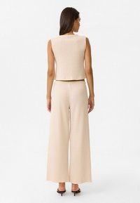 Beiges strukturiertes zweiteiliges Outfit, bestehend aus einem ärmellosen Crop-Top und weiten Hosen. Die Hosen haben einen lockeren Schnitt und einen elastischen Bund.