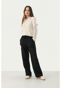 Kermanisa ribbed knit cardigan dengan kancing depan, dipadukan dengan celana hitam longgar dengan pinggang elastis dan sepatu sneakers putih dengan sol cokelat.