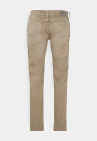 Jeans de mezclilla elástica beige con un corte slim, con dos bolsillos traseros, trabillas para cinturón y una etiqueta en la cintura. Textura suave con un ligero brillo.