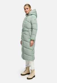 Puffjacka i mjuk mintgrön färg, med huva, oversized passform, bälte vid midjan och horisontell quiltning. Bärs med beige snörda stövlar.