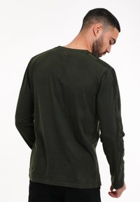 Camicia a maniche lunghe in cotone verde scuro. Presenta un collo a girocollo, polsini a coste e una sottile trama sulle spalle.