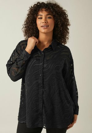 Blusa nera realizzata in tessuto trasparente con una texture ondulata. Presenta un'apertura con bottoni sul davanti, maniche lunghe e una vestibilità rilassata.