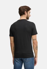 Camiseta de algodón negra con un clásico cuello redondo, mangas cortas y una textura suave, mostrada desde la parte de atrás, combinada con unos pantalones vaqueros azules.