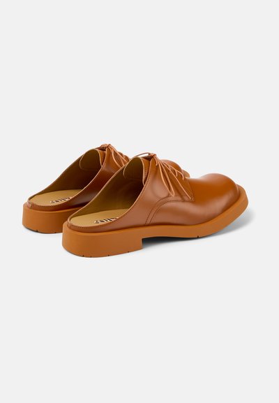 Bruna läder slip-on skor med runda tår, elastiska snörningar och tjocka orangea gummisålar. Slät textur med en minimalistisk design.
