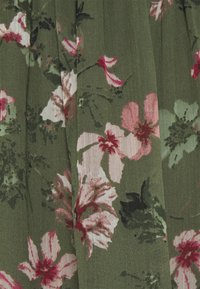 Blommönstrad tyg med grön bakgrund och rosa samt vita blommor. Materialet har en mjuk textur med subtila veck och en naturlig fall.
