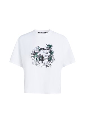 T-shirt blanc avec un dessin noir et vert représentant une personne debout près d'une balustrade surplombant l'eau, un voilier, des palmiers et des bâtiments au loin.