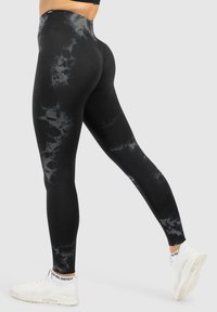 Leggings neri a vita alta con un motivo a marmo in diverse sfumature di grigio, realizzati in un tessuto elasticizzato, abbinati a scarpe sportive bianche.