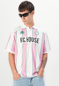 Biała i różowa w paski koszulka polo z krótkim rękawem z zielonymi detalami, z logo "F.C. HOUSE" i brandingiem Kappa. Założone dżinsowe szorty.