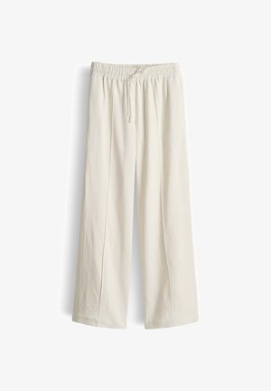 Roomy crèmekleurige broek met elastische tailleband en trekkoord, plat uitgespreid tegen een witte achtergrond.