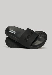 Zwarte slidesandalen met een brede band waarop de merknaam is gedrukt, een geprofileerde voetbed en een patroon op de zool voor grip.