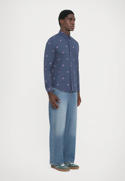Marineblå skjorte med små rosa blomsterprint, knapp-ned krage, lange ermer, kombinert med lyse blå vide jeans og grønne joggesko.