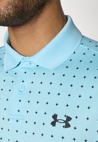 Polo de culoare albastru deschis, cu un material texturat, un model cu stele negre, nasturi în contrast și un logo negru embosat pe piept.