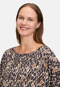 Top w panterkę w odcieniach brązu i granatu, z szerokim dekoltem i ozdobiony małymi ćwiekami. Wykonany z miękkiego, teksturowanego materiału.