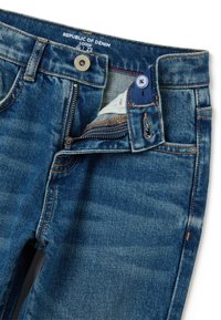 Jeans de denim azul de corte holgado con cierre de botón, cremallera y un patrón teñido de hilo con detalles de costura en contraste.