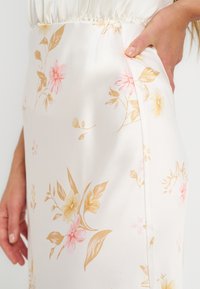 Χέρι γυναίκας που ξεκουράζεται στην τσέπη λευκής φούστας με κίτρινο και ροζ λουλουδάτο σχέδιο και ελαστική μέση.