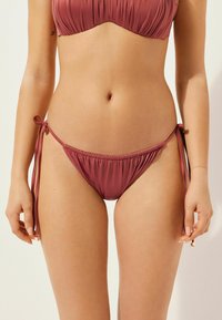 Conjunto de bikini en color rosa apagado, que presenta un top fruncido y una parte inferior con lazo lateral. Tela suave con lazos ajustables para un ajuste personalizable.