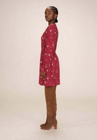 Robe florale rouge à manches longues, avec une coupe décontractée et un col à volants. Associée à des bottes à talons en daim marron, montantes jusqu'au genou.