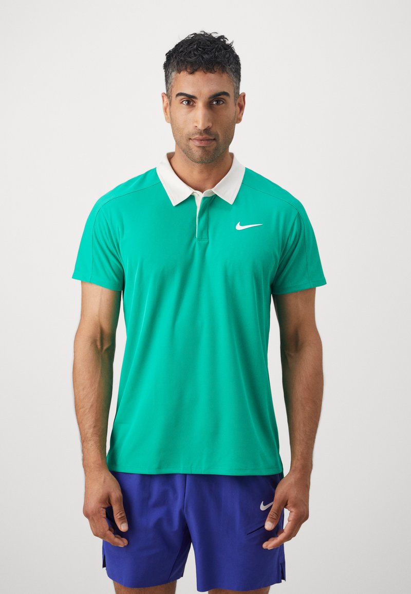 Roheline polo särk valge kraega ja Nike logo. Lühikesed varrukad, sile tekstuur, koos lilla lühikesed püksid. Lihtne ja sportlik disain.