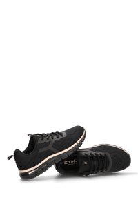 Zapatillas deportivas negras con una parte superior de malla texturizada, acentos suaves en contraste y una suela acolchada que presenta un sutil logotipo a lo largo del costado.