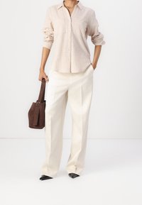 Chemise boutonnière beige clair à manches longues, associée à un pantalon crème taille haute et un sac à main en suède marron. Chaussures noires à bout pointu.