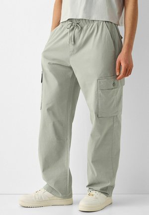 Pantalones cargo verde claro con bolsillos laterales, cinturilla elástica con cordón, combinados con zapatillas blancas y una camiseta blanca de manga corta.