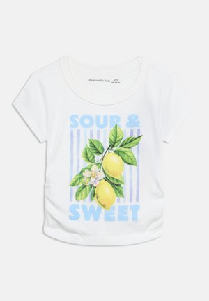 Λευκό παιδικό μπλουζάκι με μπλε κείμενο "Ξινό και Γλυκό" και εικονογράφηση δύο λεμονιών με πράσινα φύλλα και λευκά λουλούδια σε ριγέ φόντο.