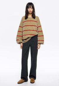 Beżowy sweter dzianinowy w czerwone poziome paski, luźny krój, połączony z szarymi szerokimi spodniami i beżowymi klapkami z detalem klamry.
